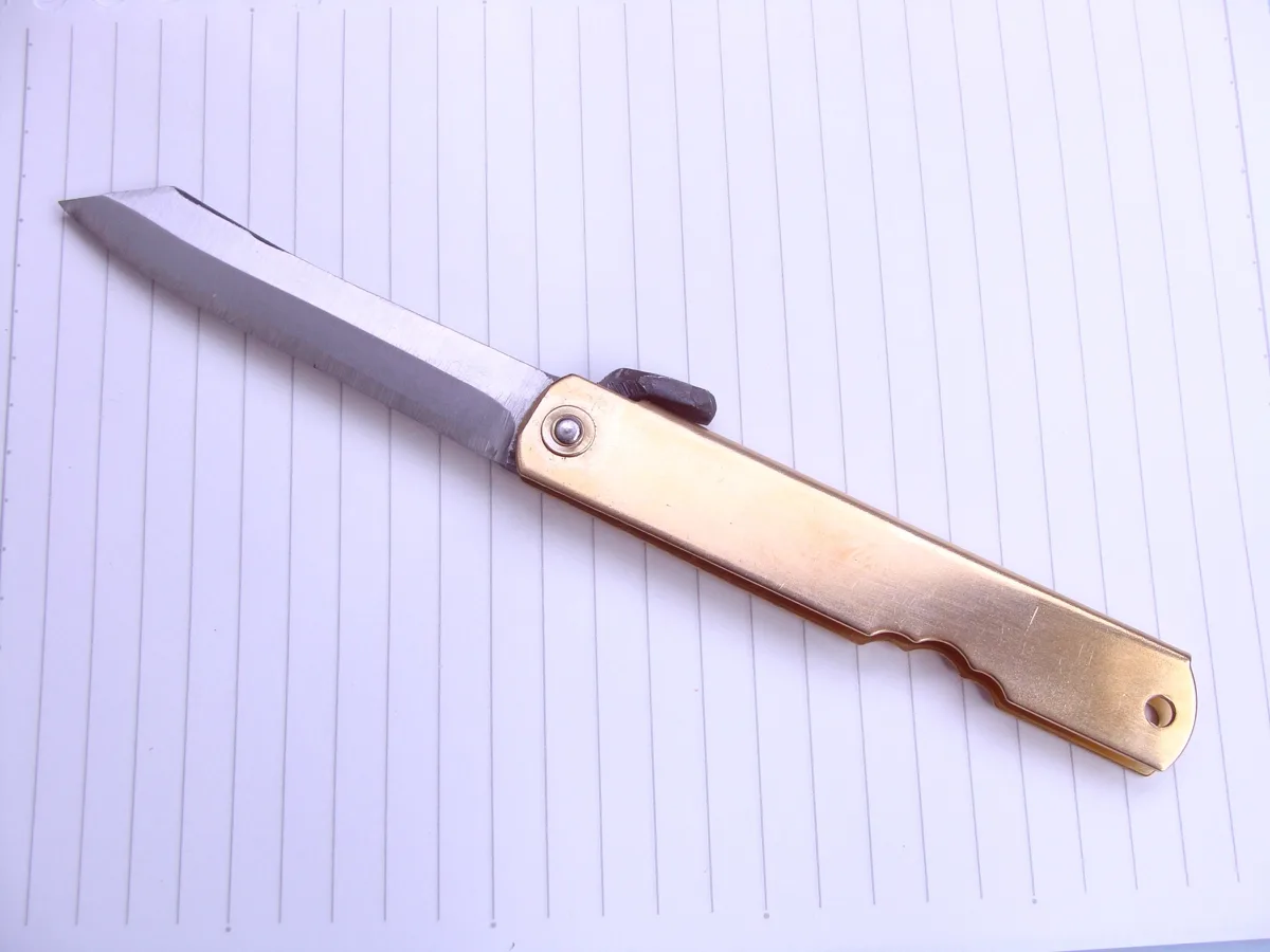 Open Higonokami Aogami Dai folding knife with brass handle on lined paper