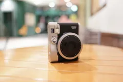 Black and silver Fujifilm instax mini 90 camera on a wooden table, with mini 90 marking visible