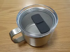 Silver MUJI graduated stainless-steel mug with transparent sliding lid on a wooden surface