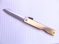 Open Higonokami Aogami Dai folding knife with brass handle on lined paper